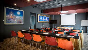 A conference room with a long table, orange chairs, a projector screen, and a large painting on the wall.