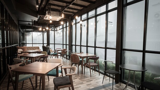 Un restaurante moderno con mesas y sillas de madera, ventanas amplias y lámparas colgantes.
