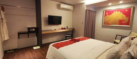 Una habitación de hotel con cama, escritorio, televisor y aire acondicionado.