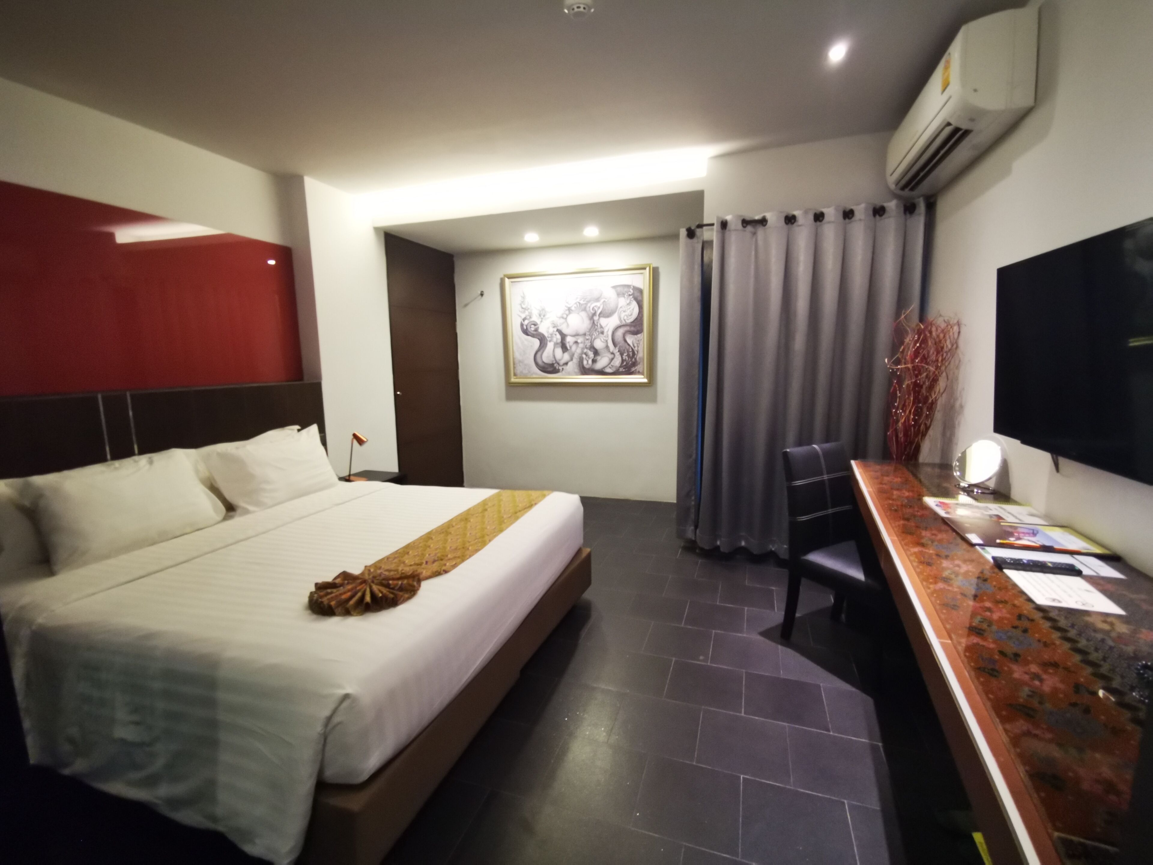 A hotel room with a bed, a desk, a chair, a television, and an air conditioning unit.