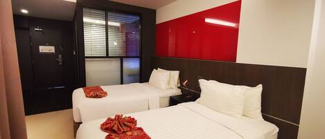 Quarto de hotel com duas camas, uma parede de destaque vermelha e uma janela com persianas.