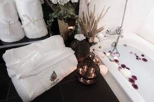 A bathroom with a bathtub, towels, a decorative vase, and candles.