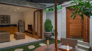 Un espacio comedor al aire libre acogedor, con mobiliario de mimbre, una mesa redonda y velas.
