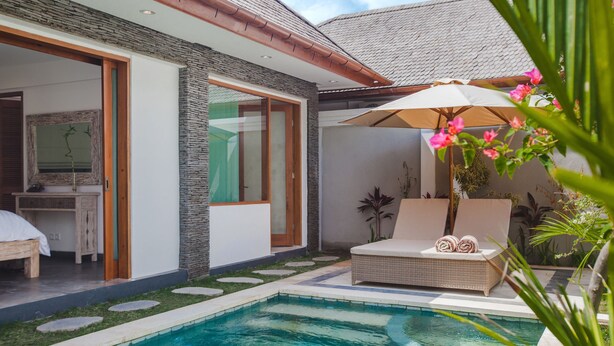 Un área de piscina moderna al aire libre con una silla de salón y una sombrilla, un pequeño jardín y una vista parcial de un dormitorio con cama y escritorio.