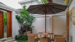 Un patio con mobiliario de mimbre, una mesa dispuesta para dos personas y una sombrilla.