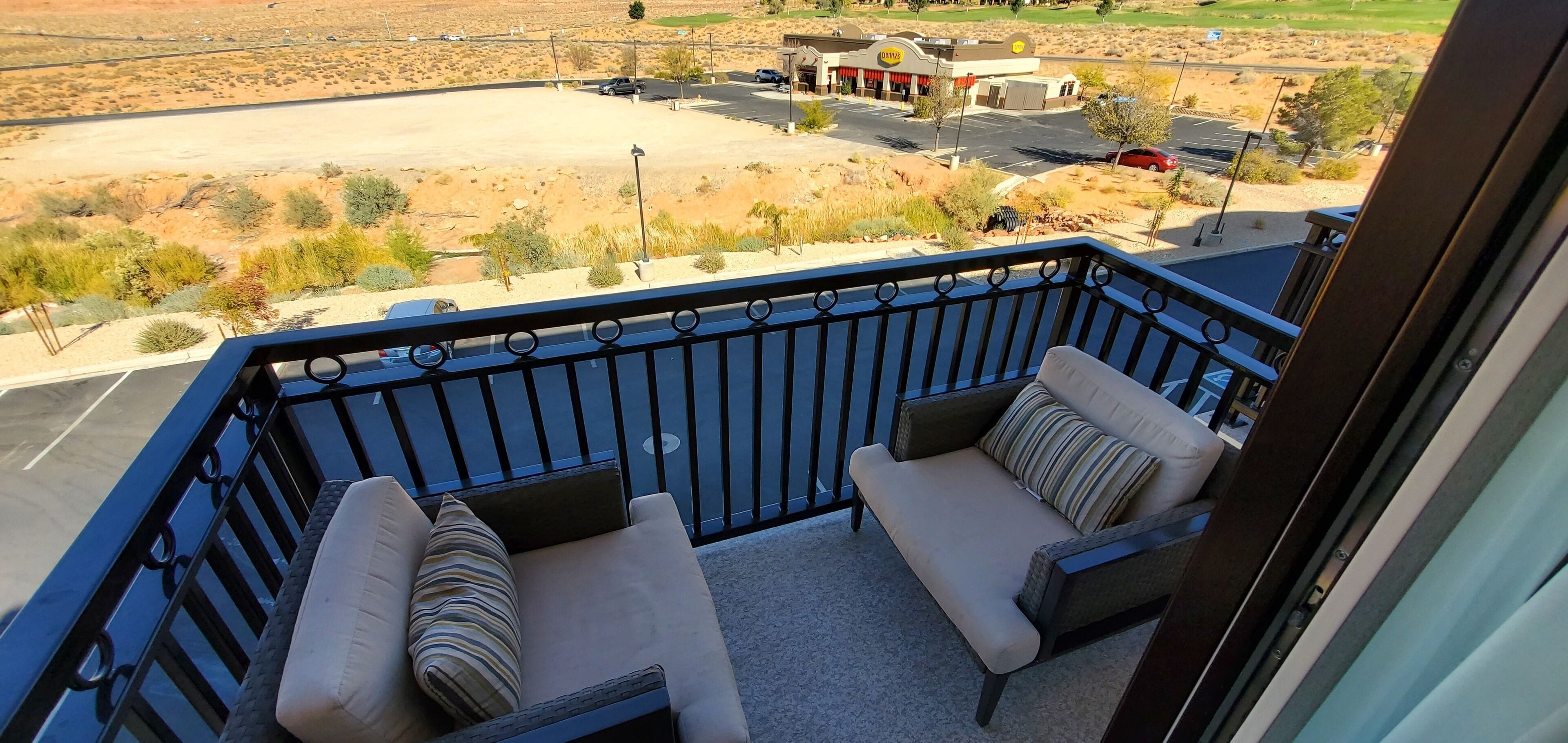A balcony with two cushioned chairs and a view of a parking lot and a gas station.