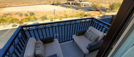 A balcony with two cushioned chairs and a view of a parking lot and a gas station.