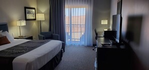 Hotellihuone, jossa on sänky, työpöytä, tuoli, televisio ja ikkuna, jossa on verhot.