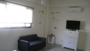A room with a bed, a dark sofa, a white dresser, a television, and a small plant. - Penghu 123 V-Stone Inn (Magong)