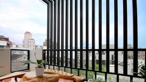 A balcony with a wooden table, a potted plant, and a view of buildings through metal bars. - Penghu 123 V-Stone Inn (Magong)