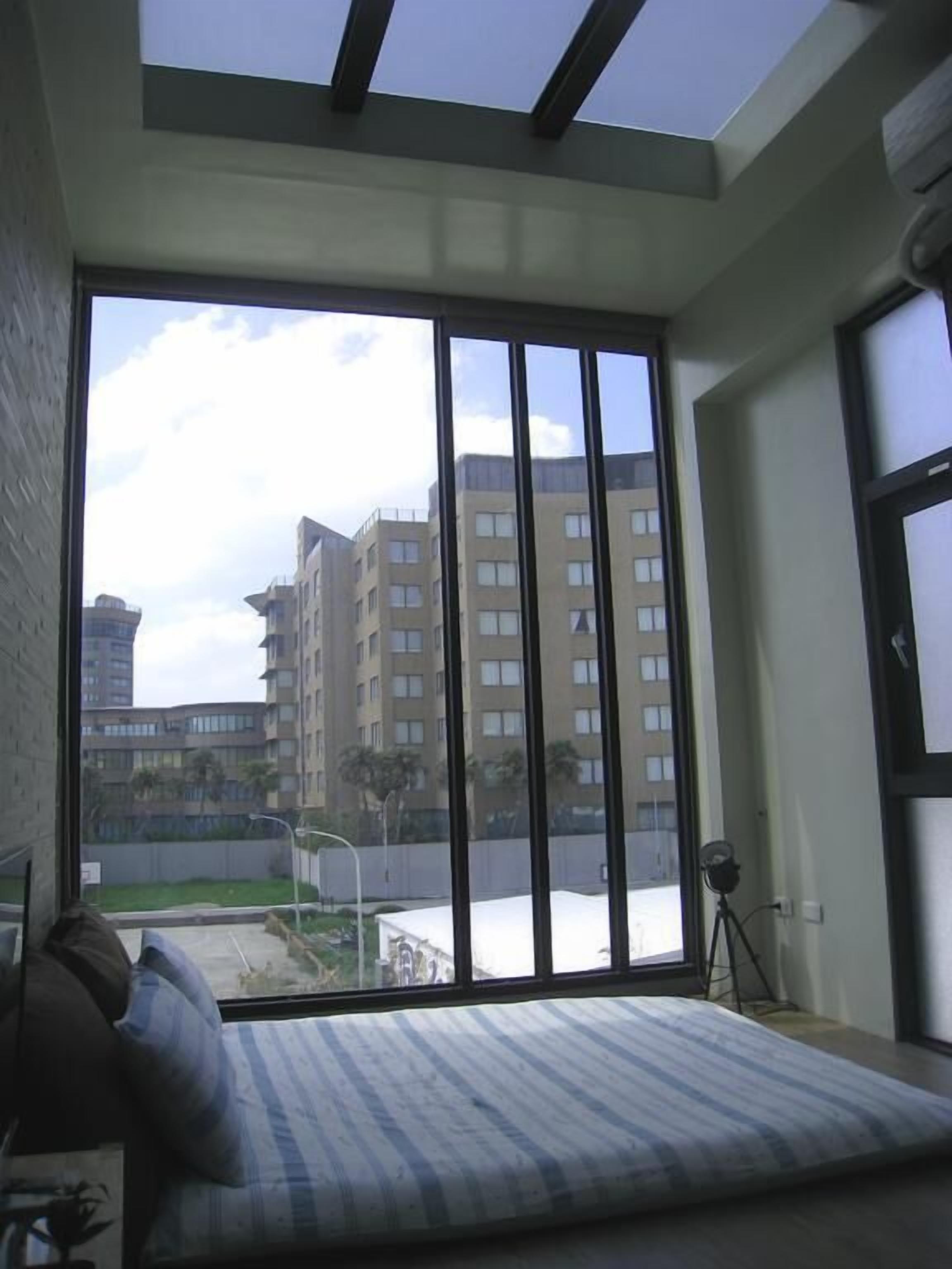 A room with a large window, a bed with striped bedding, and a tripod lamp.