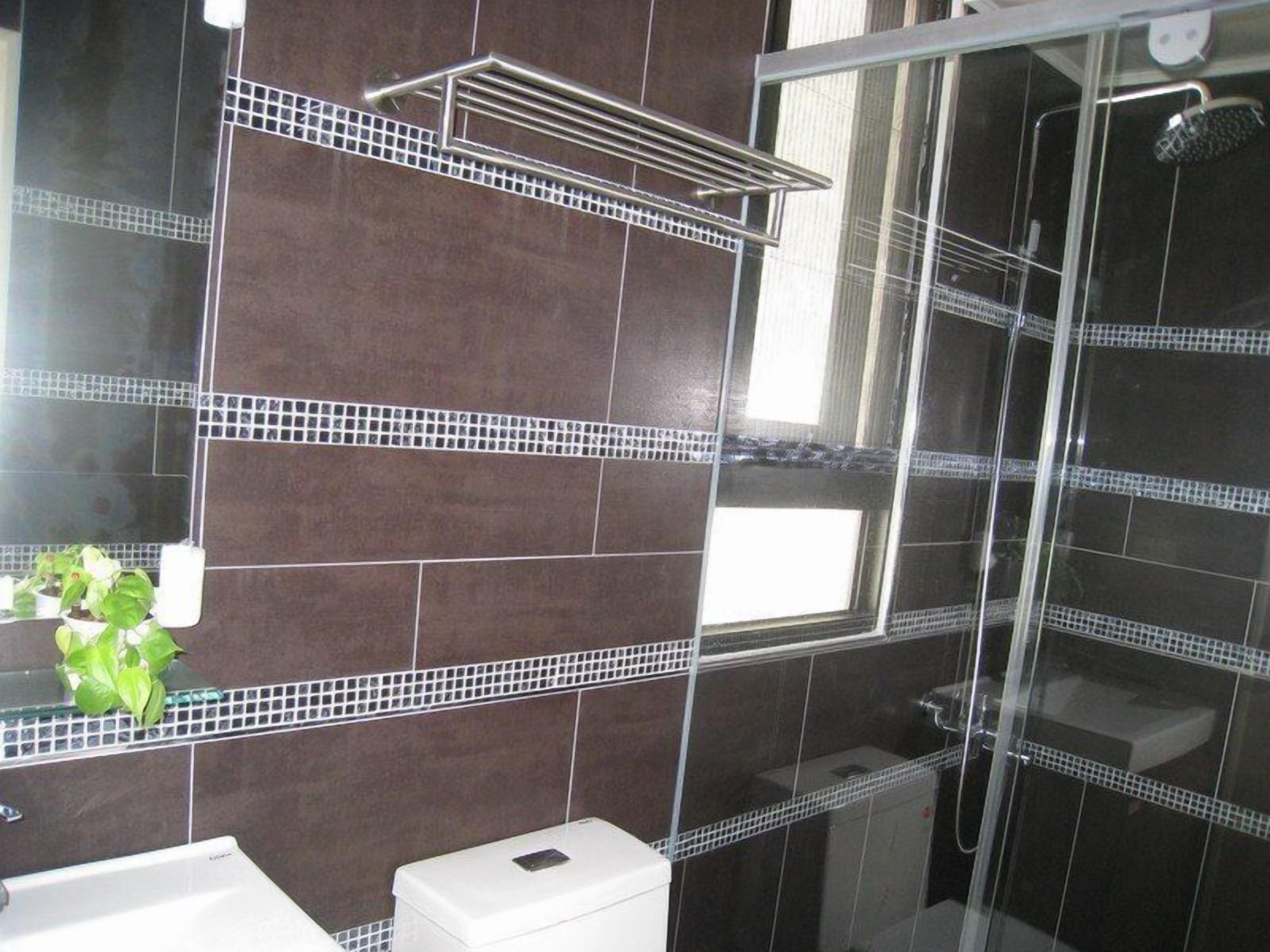 Un baño con baldosas oscuras, cabina de ducha de cristal y un inodoro blanco.