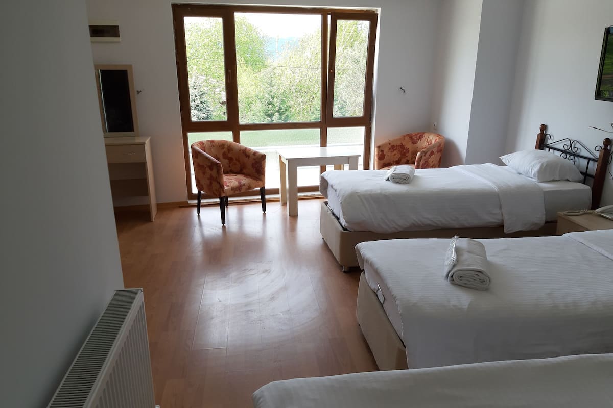 A hotel room with two beds, a chair, a small table, and a window with a view of greenery.