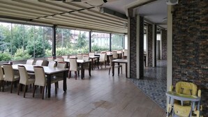 A spacious dining area with tables and chairs, large windows offering a view of greenery, and a high ceiling with exposed beams. - The Hotel Sapanca (Sapanca)