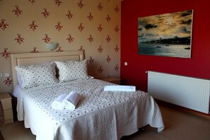Una cama bien hecha con colcha, un cuenco en la mesita de noche y un cuadro de un atardecer en la pared.
