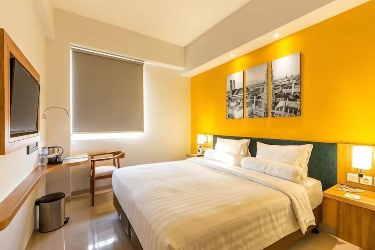 A hotel room with a bed, bedside tables, a TV, a window, and artwork on the wall.