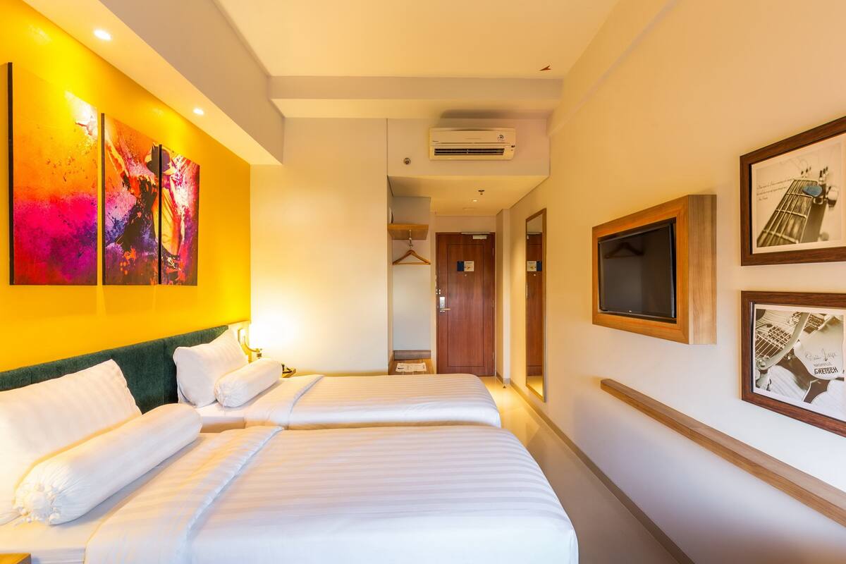 A hotel room with two beds, a large abstract painting on the wall, and a framed picture on the wall.