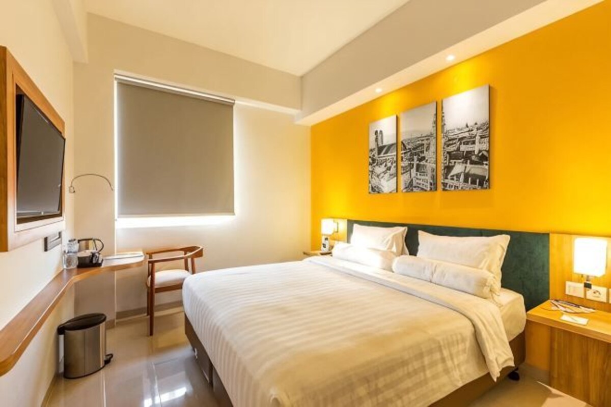 Habitación de hotel con cama, mesitas de noche, televisor, ventana y cuadros en la pared.