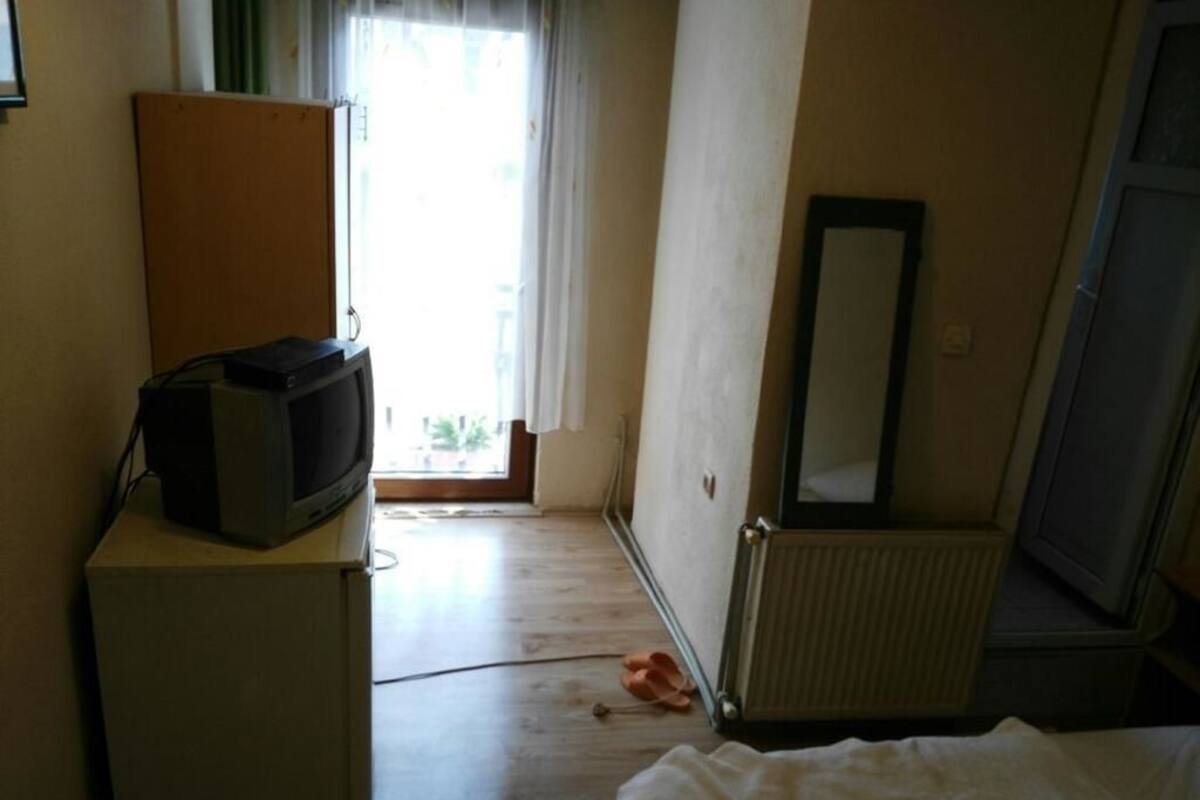 A room with a television on a stand, a radiator, a mirror, and a pair of slippers on the floor.