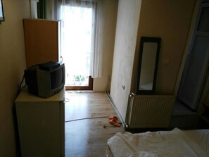 Une pièce avec un téléviseur posé sur un meuble, un radiateur, un miroir et une paire de chaussons sur le sol.