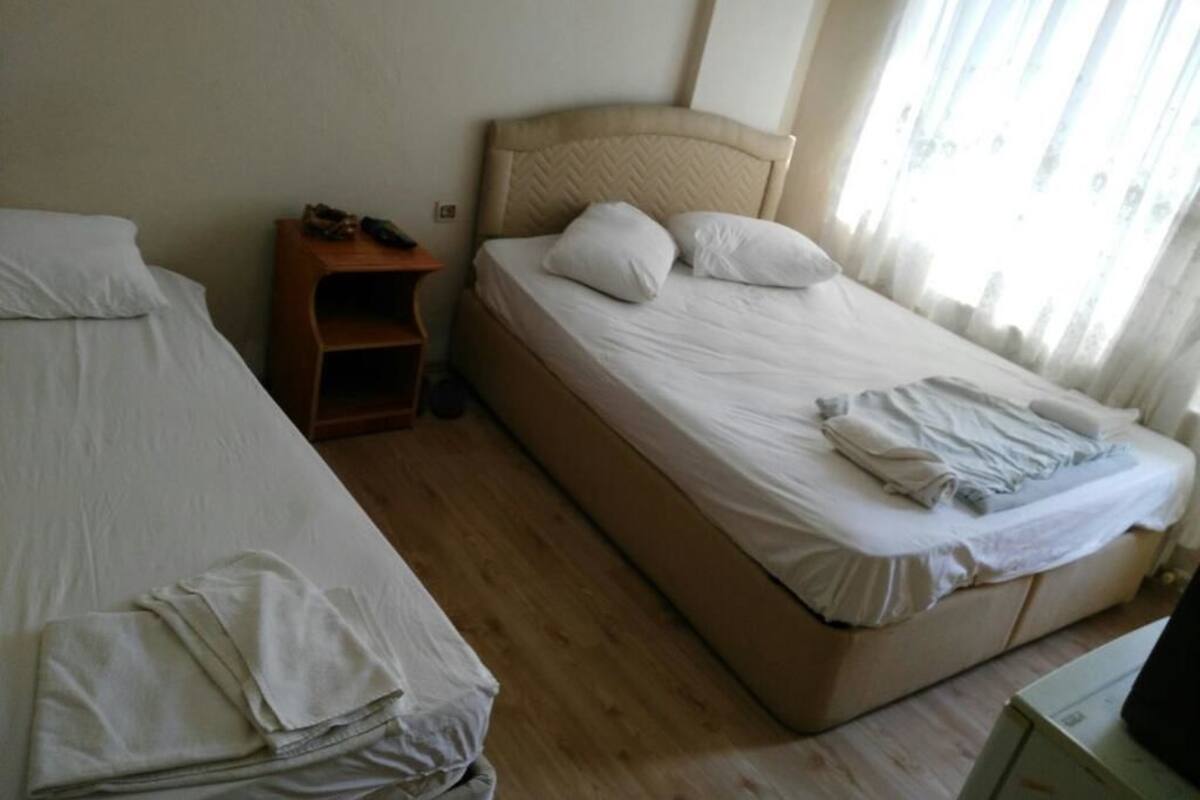 A hotel room with two single beds, a wooden nightstand, and a large window with curtains.