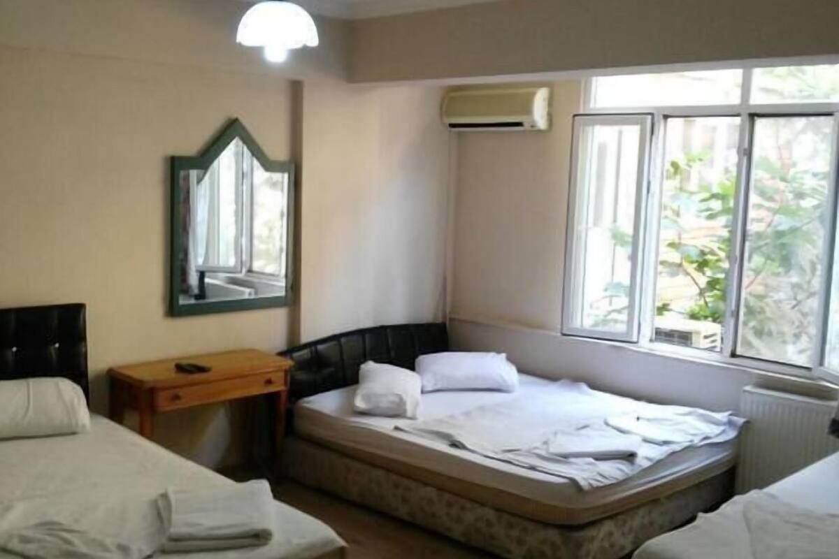 A hotel room with two beds, a wooden floor, a ceiling fan, a window with a view, and an air conditioning unit.