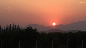 Solnedgang over et bjerglandskab med et hegn i forgrunden.