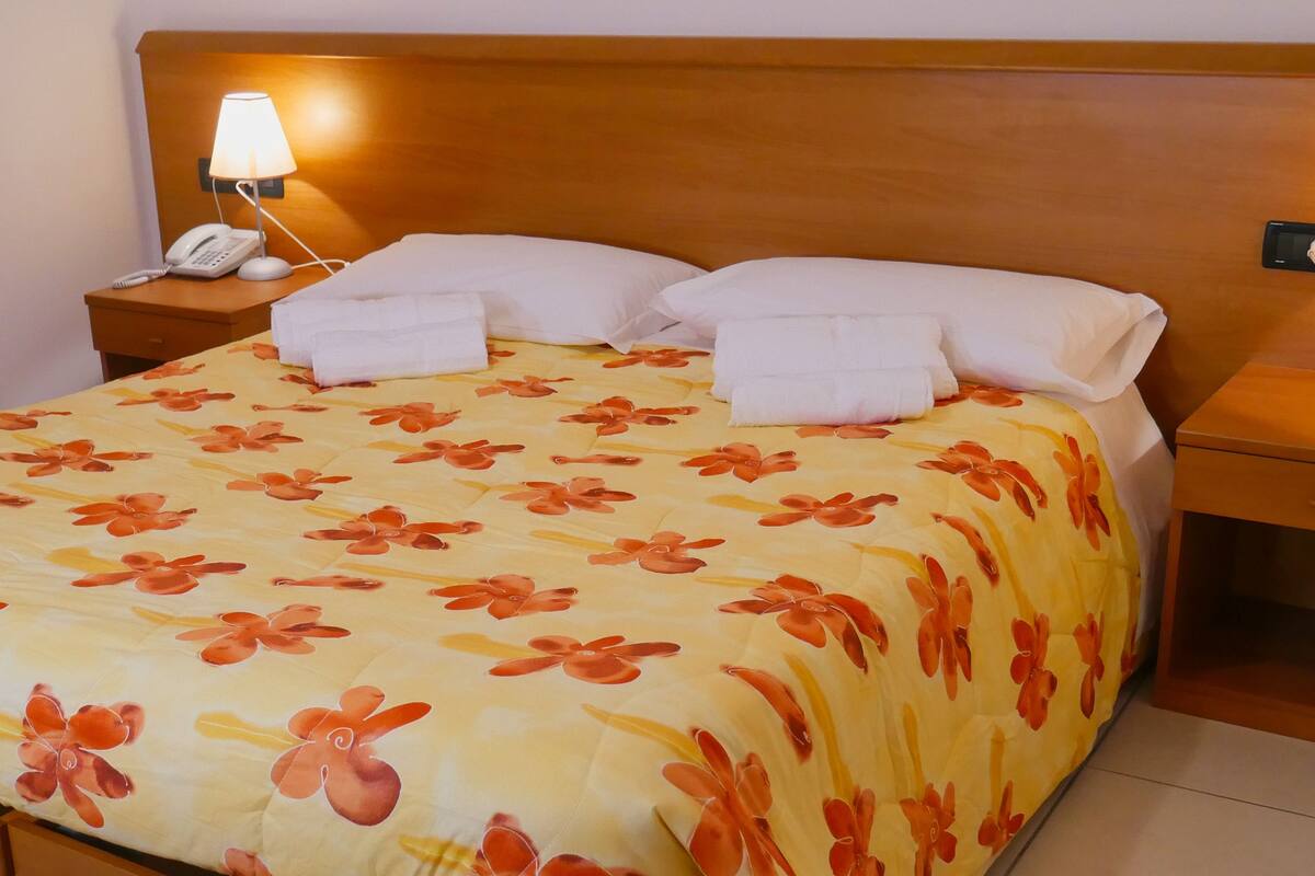 A hotel room with a bed, two bedside tables, a telephone, and two lamps.