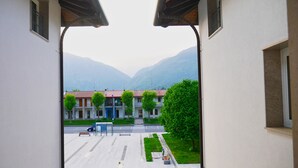 A view from a building's entrance to a street with a bus stop, a bench, and a tree-lined sidewalk. - Hotel Vajont (Vajont)