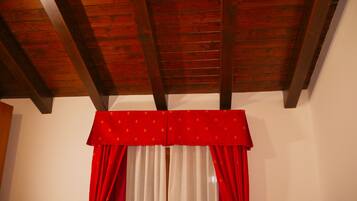 A room with a wooden ceiling, red curtains, and white blinds.