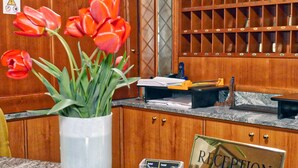 A reception desk with a clear sign, a vase of red tulips, and a wooden cabinet with a wine rack in the background. - Hotel Vajont (Vajont)