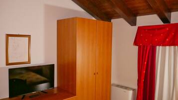 A room with a wooden wardrobe, a framed artwork on the wall, a television, and a radiator.