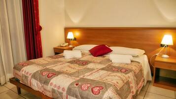 A neatly made bed with a patterned bedspread, two bedside lamps, a wooden headboard, and a red pillow.
