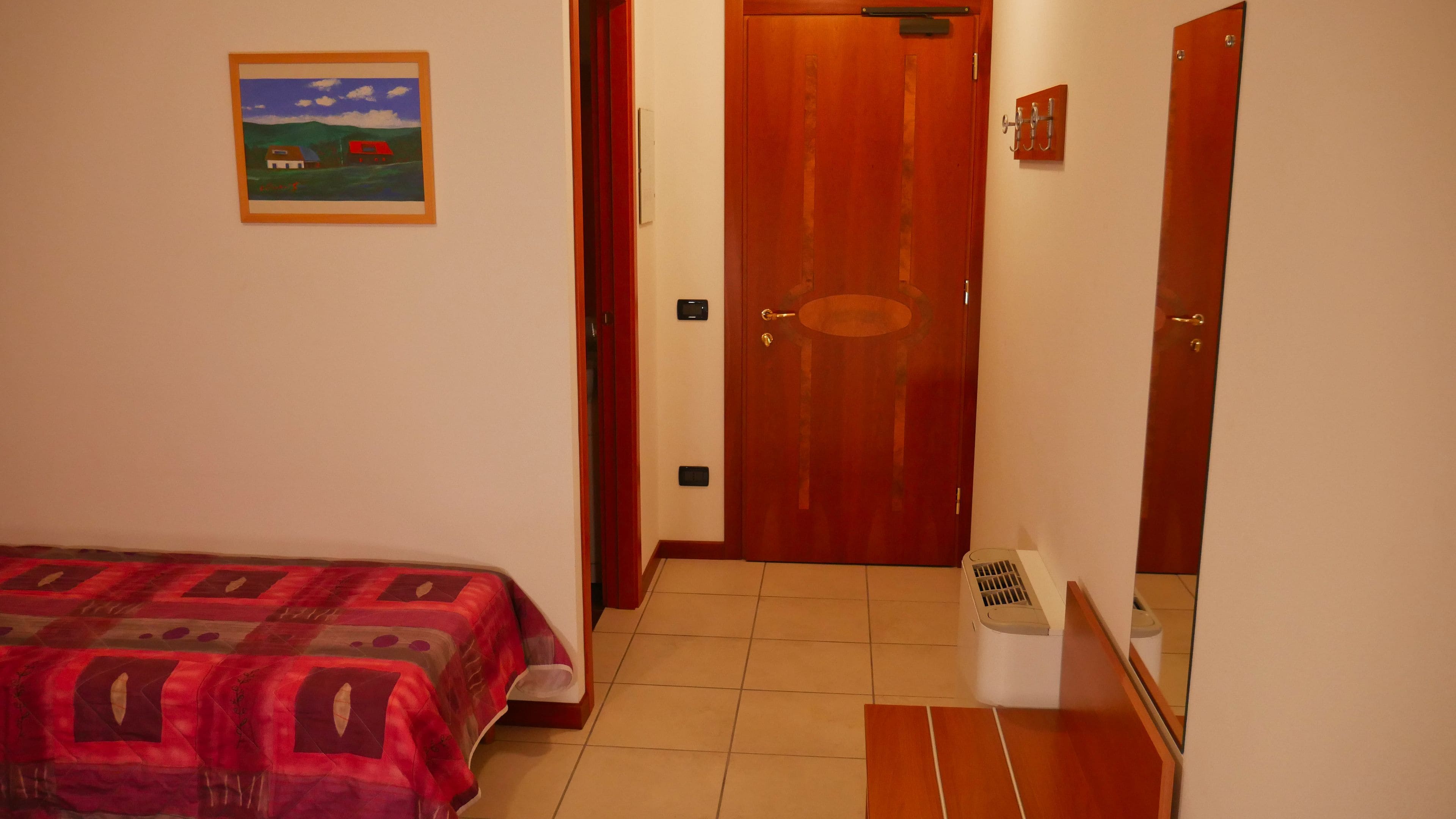 A bedroom with a bed, a door, a small window, and a wall-mounted picture.