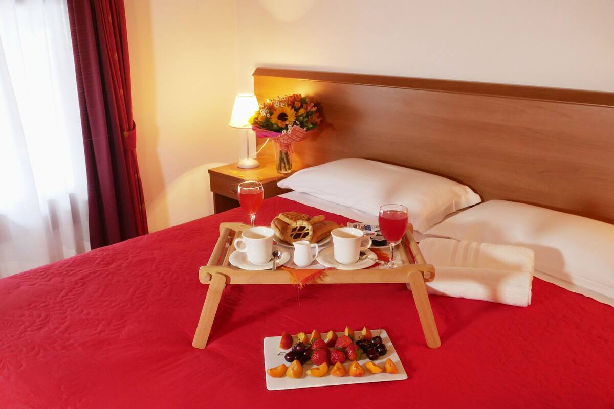 A neatly made bed with a red bedspread, a tray with breakfast items, and a fruit plate.