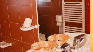 Une salle de bain avec un lavabo blanc, des toilettes blanches et un porte-serviettes blanc. On trouve deux paniers en osier sur le comptoir du lavabo.