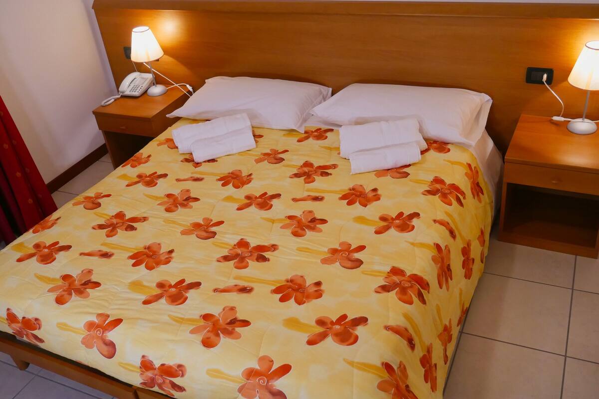 A hotel room with a bed, two bedside tables with lamps, a telephone, and a red curtain.