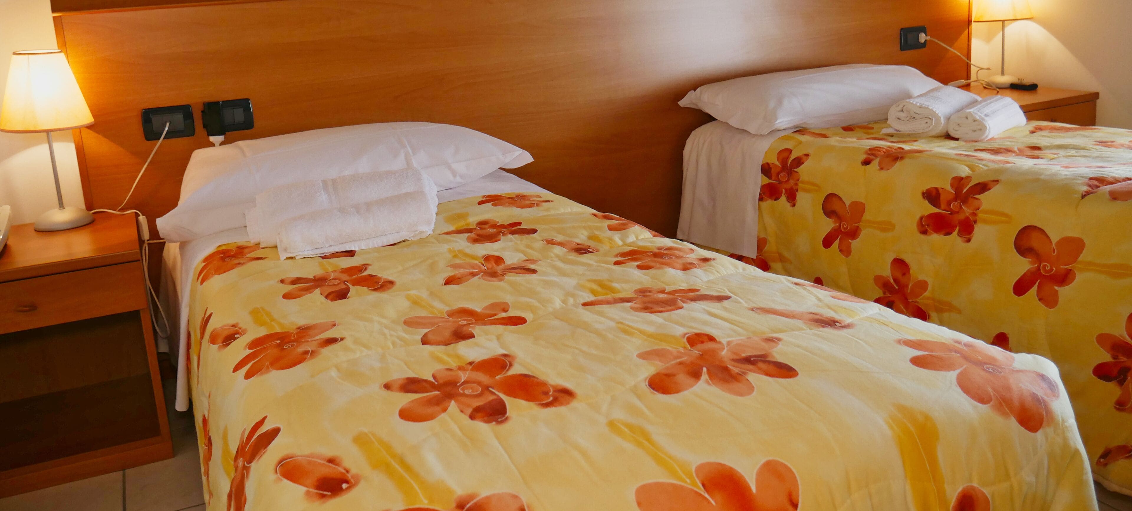 Two single beds with floral bedding, bedside lamps, and a wooden headboard.