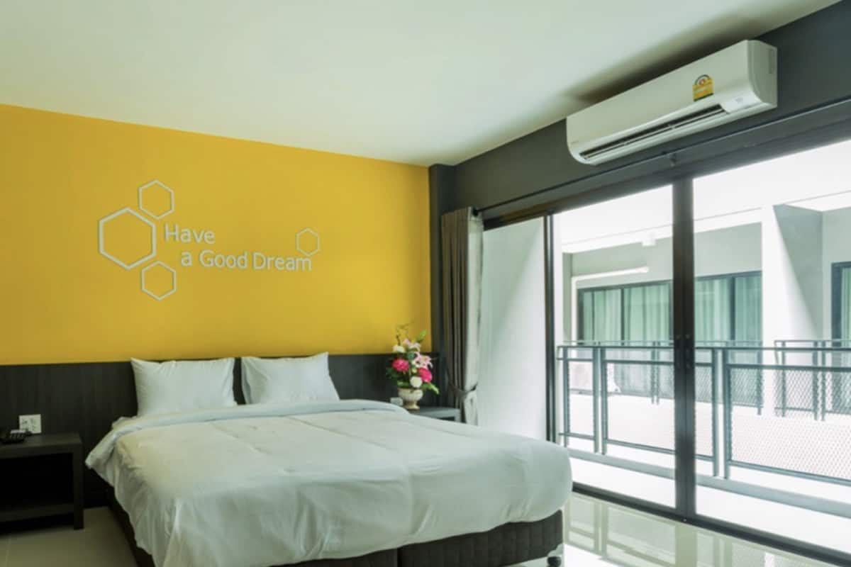 Una habitación de hotel moderna con una cama grande, una mesita de noche, un aire acondicionado instalado en la pared y vistas al exterior a través de un ventanal amplio.