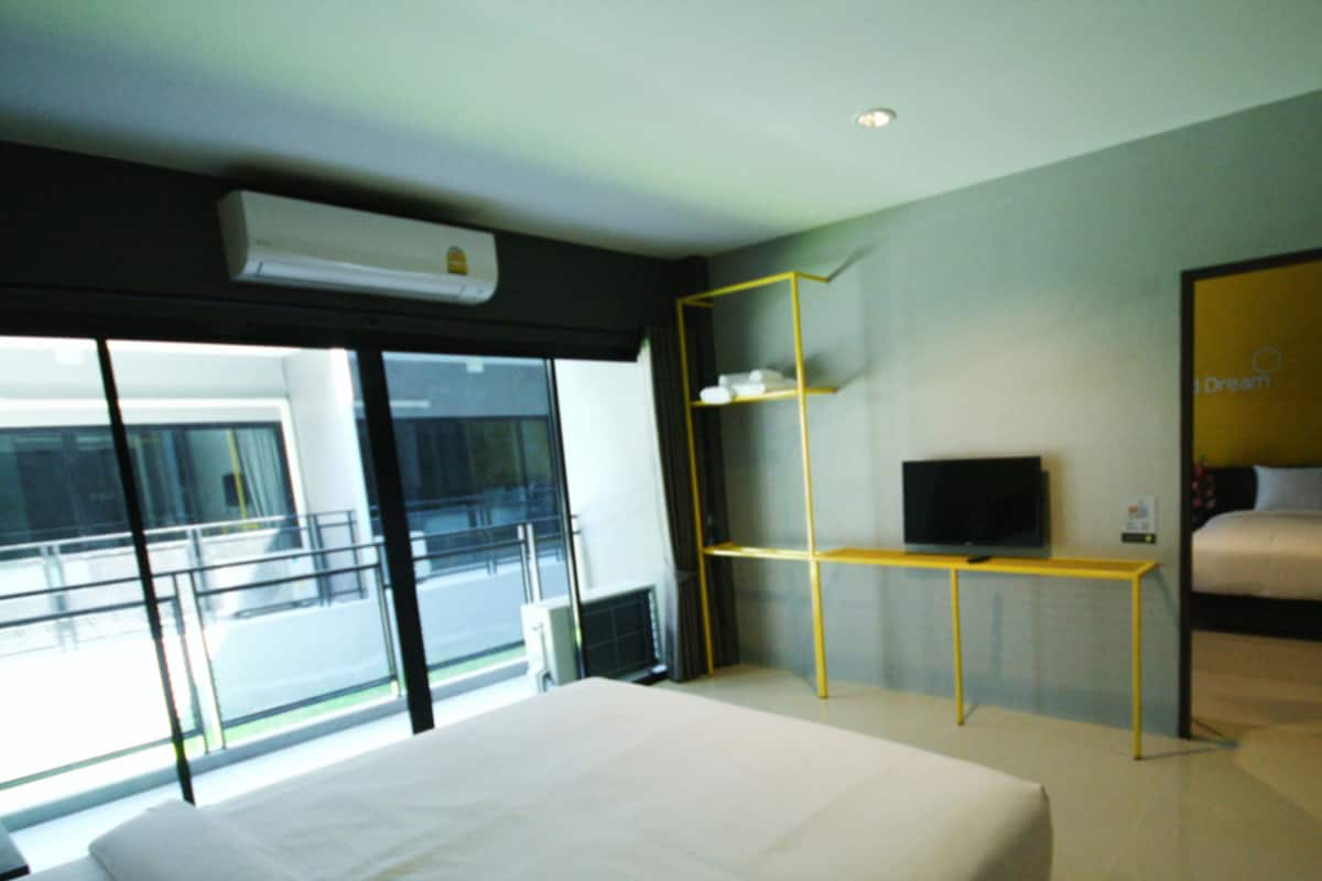 Una habitación de hotel moderna con una cama grande, un televisor sobre un mueble bajo, un escritorio y un balcón con vistas.