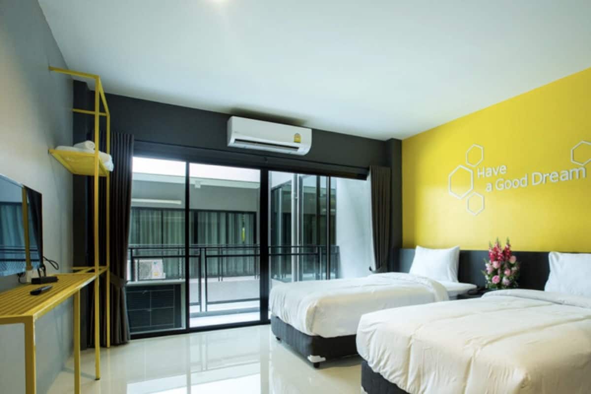 Habitación de hotel moderna con dos camas, un balcón y una pared de acento amarilla con una cita motivacional.
