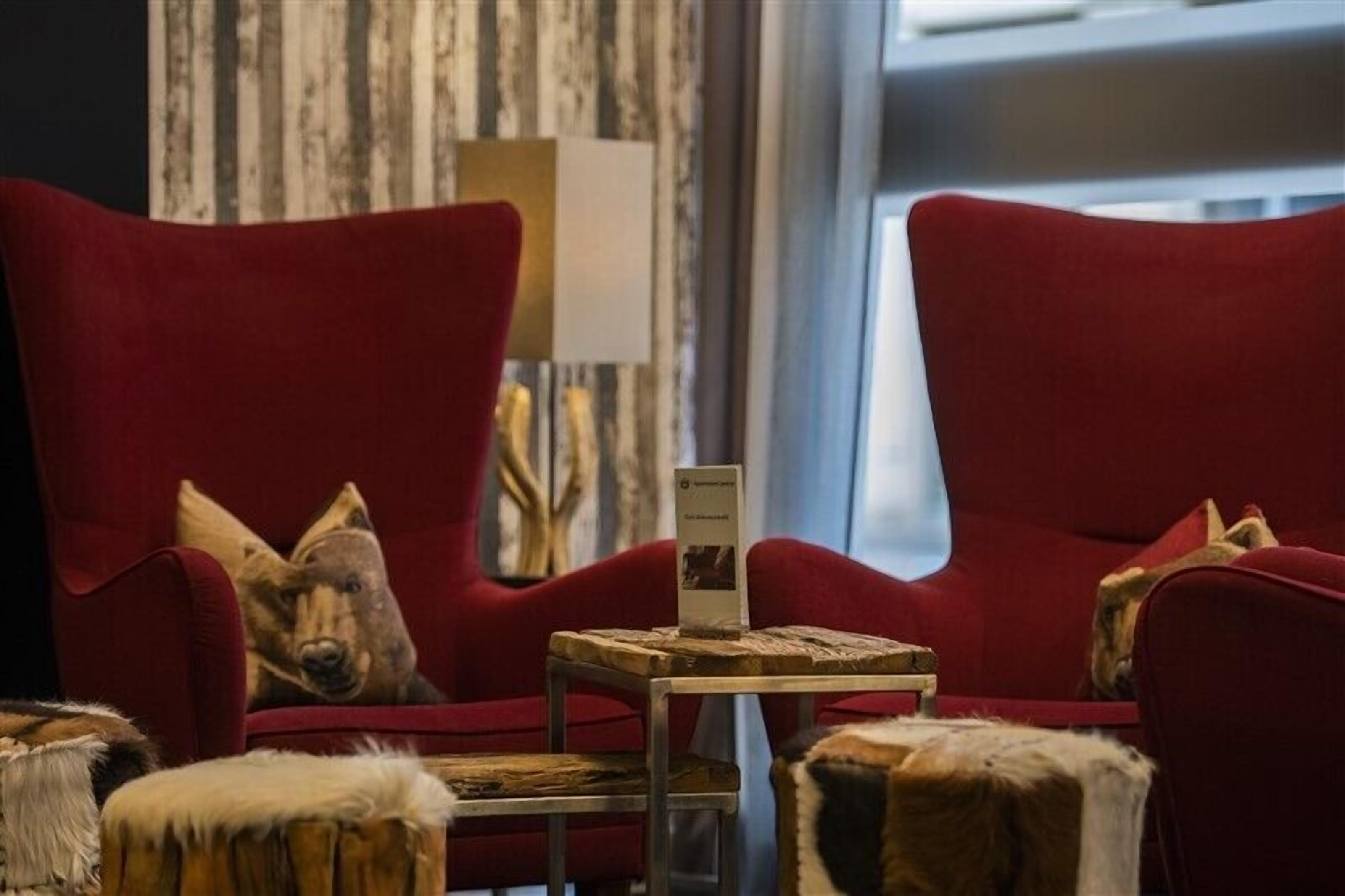 Een kamer met twee rode fauteuils, een klein houten tafeltje met een bord en een poef bekleed met bont.