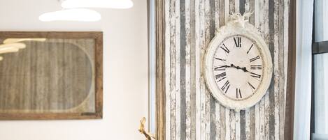 Une pièce avec une grande horloge au mur, un miroir à cadre en bois et un luminaire moderne.