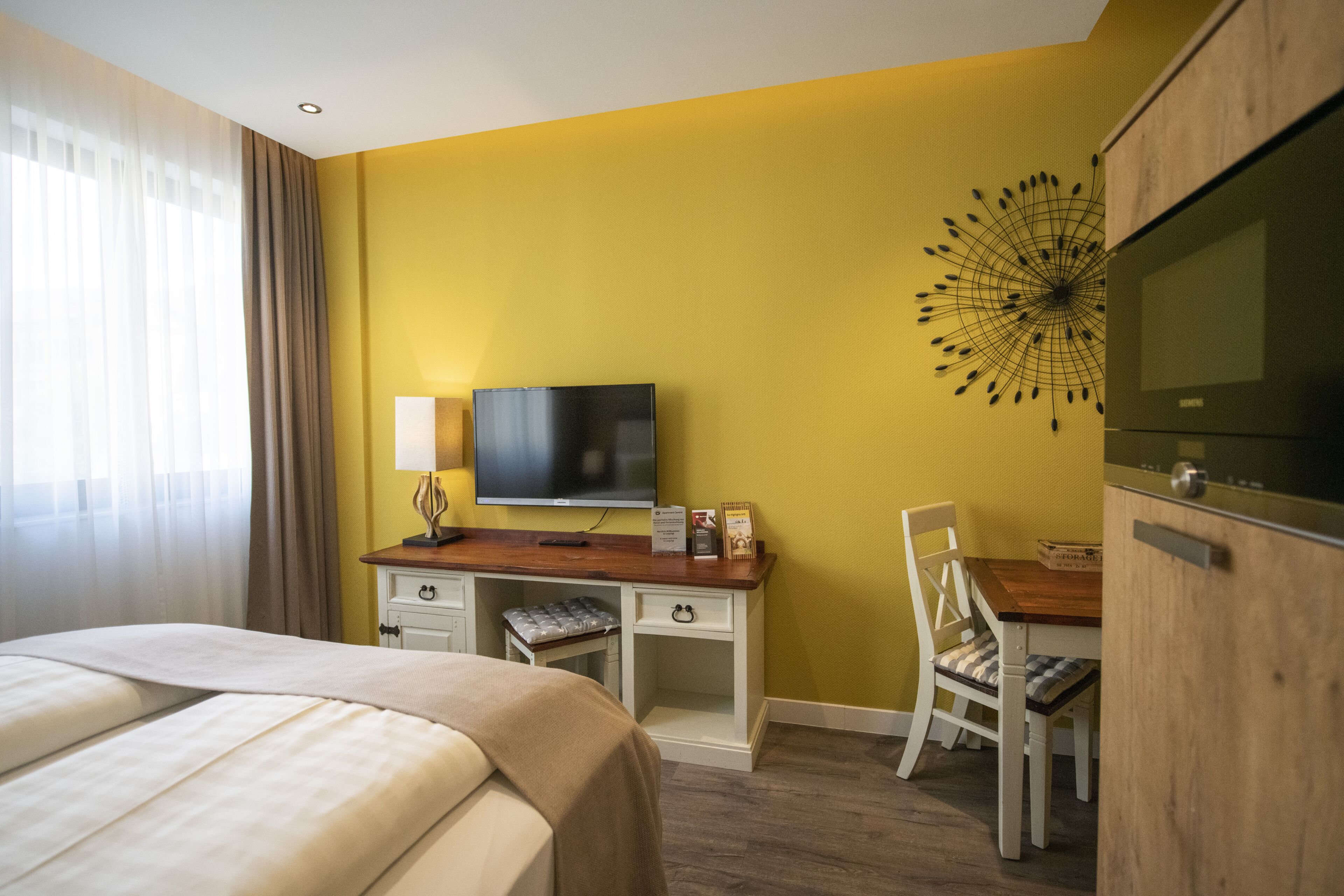 A hotel room with a bed, a desk with a TV, a chair, and a wooden cabinet.