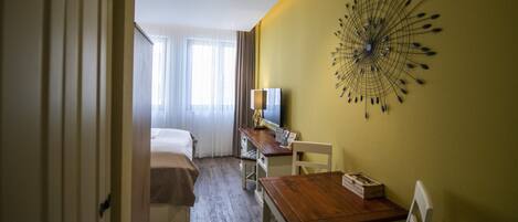 A hotel room with a bed, a desk with a chair, a television, and a wall decoration.