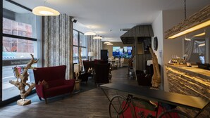 Hall moderna di un hotel con un divano rosso, elementi decorativi in legno e un’area bar.