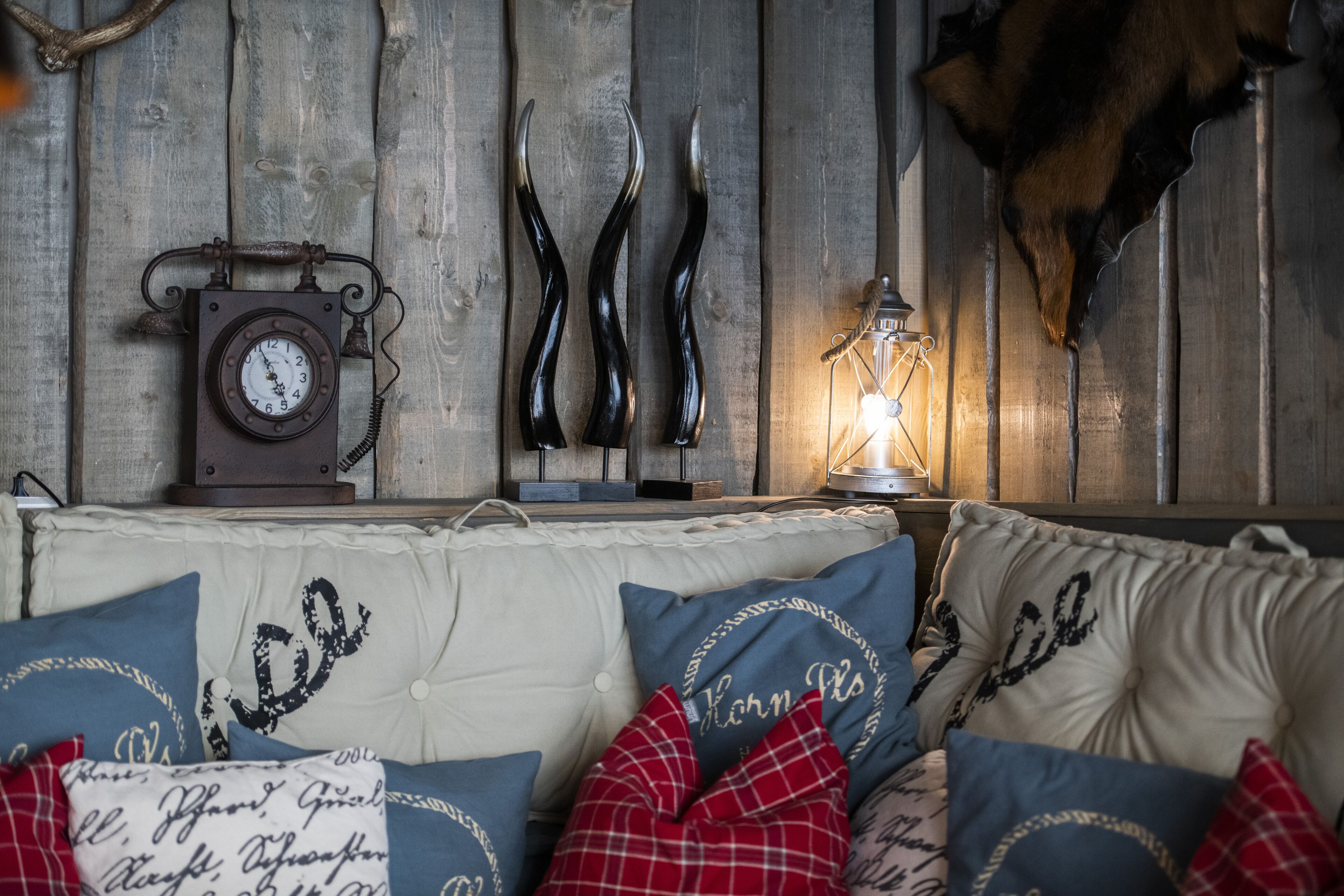 Una habitación acogedora con pared de madera, un reloj, cuernos de ciervo y una lámpara encendida.