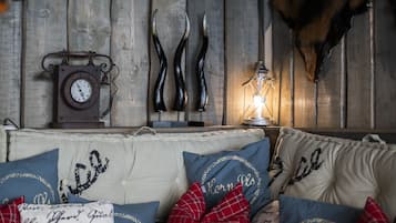 A cozy room with a wooden wall, a clock, antlers, and a lit lamp.