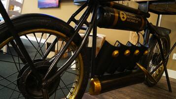 A vintage motorcycle with a black frame and gold accents, displayed indoors with a wooden floor and a painting in the background.