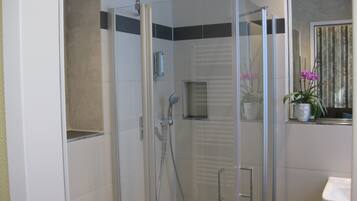 Un baño moderno con ducha de vidrio, un lavabo blanco y una orquídea en maceta en el alféizar.